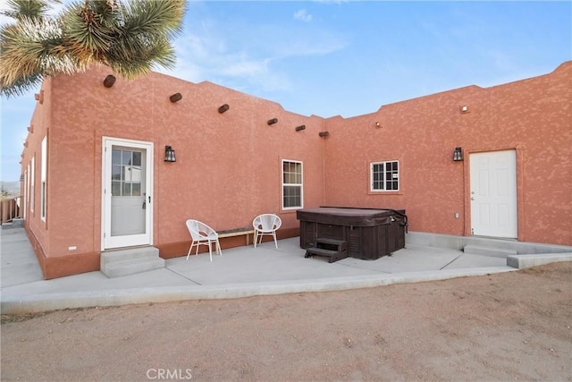 back of property with a hot tub and a patio area