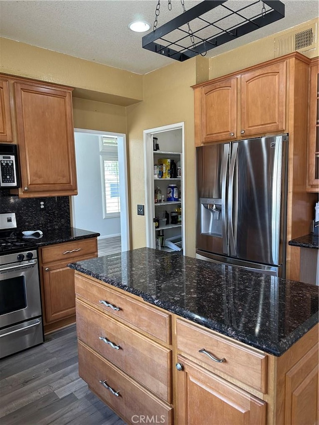 1310 Parsley Ln, Corona, CA 92879 - kitchen with appliances with stainless steel finishes, dark wood-style floors, dark stone countertops, decorative backsplash, and brown cabinets