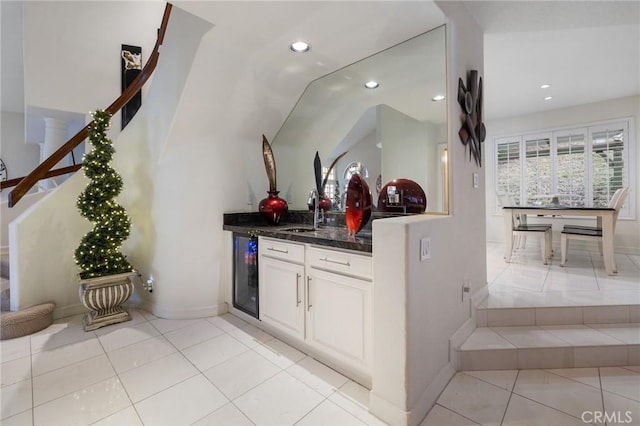 kitchen with lofted ceiling, light tile patterned floors, dark stone countertops, white cabinets, and beverage cooler