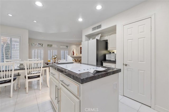 kitchen featuring a center island, light tile patterned floors, white cabinets, and refrigerator