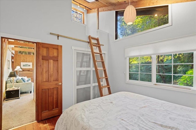 bedroom with hardwood / wood-style flooring, a towering ceiling, wood ceiling, and a skylight