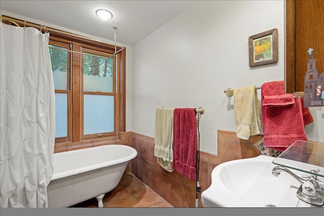 bathroom with a bathing tub, tile patterned flooring, sink, and tile walls