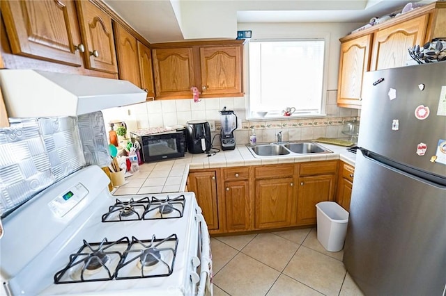 kitchen with sink, stainless steel refrigerator, white range with gas stovetop, tile counters, and decorative backsplash