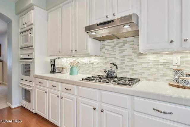 kitchen with tasteful backsplash, white cabinetry, tile countertops, and white appliances