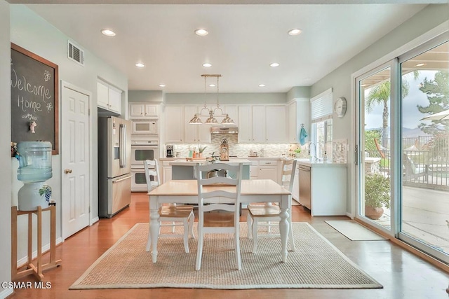 kitchen featuring decorative light fixtures, white cabinetry, backsplash, light hardwood / wood-style floors, and stainless steel appliances