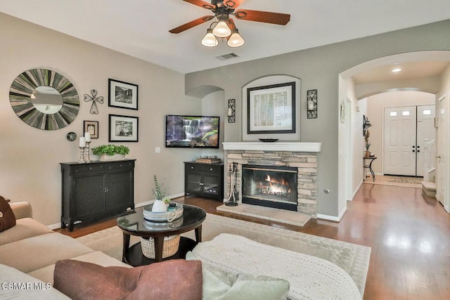 living room with a stone fireplace, light hardwood / wood-style flooring, and ceiling fan