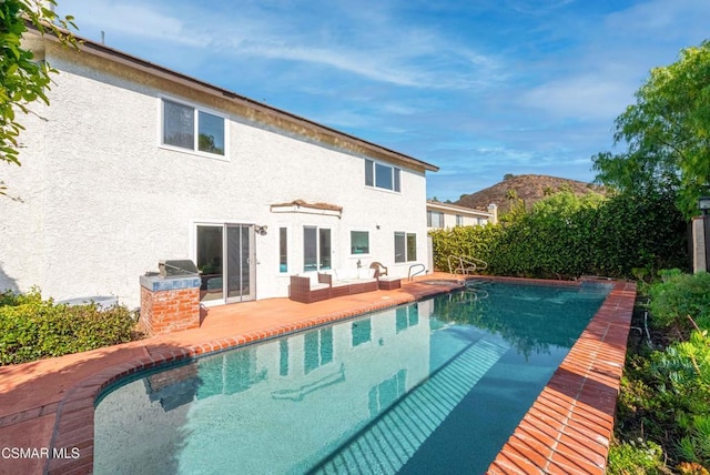 back of property with a fenced in pool, a patio, and an outdoor kitchen