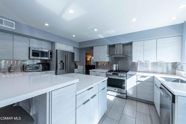 kitchen featuring sink, stainless steel appliances, a kitchen breakfast bar, decorative backsplash, and wall chimney exhaust hood