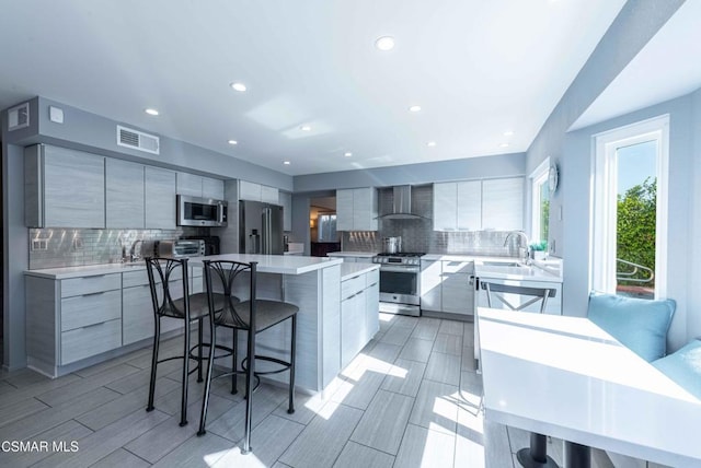 kitchen with sink, stainless steel appliances, a center island, a kitchen bar, and wall chimney exhaust hood