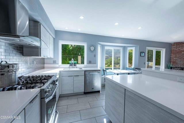 kitchen with wall chimney exhaust hood, appliances with stainless steel finishes, tasteful backsplash, and a wealth of natural light