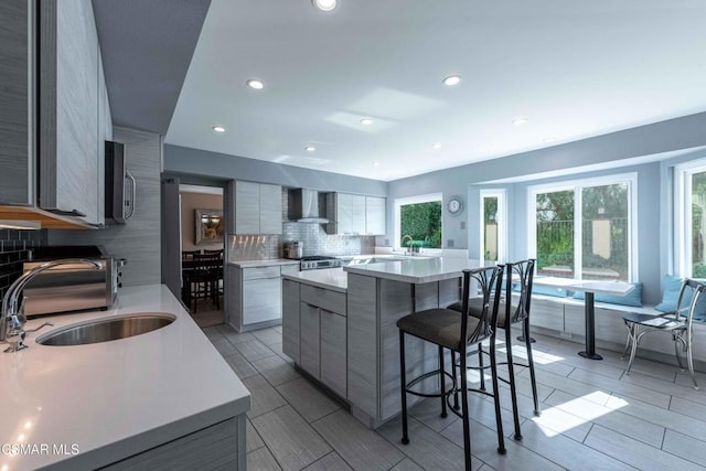 kitchen featuring sink, backsplash, stove, a center island, and wall chimney range hood