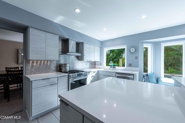 kitchen featuring wall chimney range hood, sink, light tile patterned floors, stainless steel appliances, and decorative backsplash