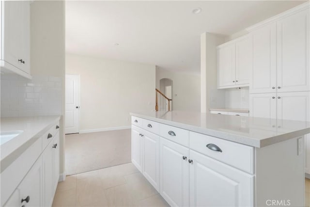 kitchen with a kitchen island, white cabinets, decorative backsplash, light stone counters, and light carpet