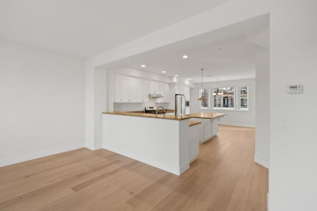 kitchen with decorative light fixtures, white cabinets, light hardwood / wood-style floors, kitchen peninsula, and stainless steel appliances