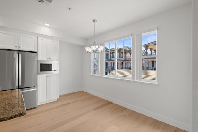 kitchen with stainless steel fridge, white microwave, light hardwood / wood-style floors, white cabinets, and a chandelier