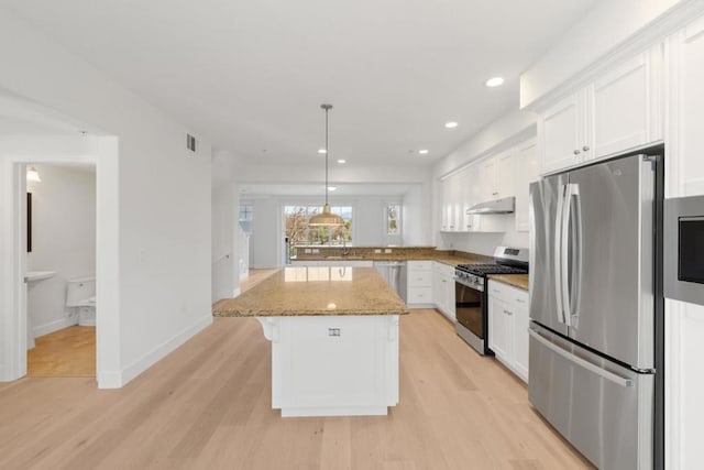 kitchen featuring appliances with stainless steel finishes, a kitchen island, white cabinetry, hanging light fixtures, and light stone countertops