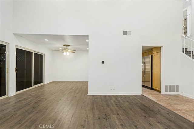 unfurnished living room featuring visible vents, dark wood finished floors, and a towering ceiling