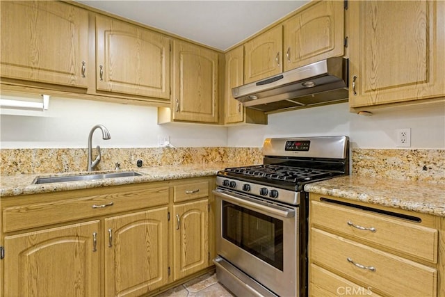 kitchen with light stone counters, under cabinet range hood, light brown cabinets, a sink, and gas stove