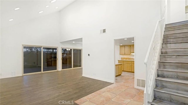 unfurnished living room with high vaulted ceiling, light wood-style flooring, stairs, and visible vents