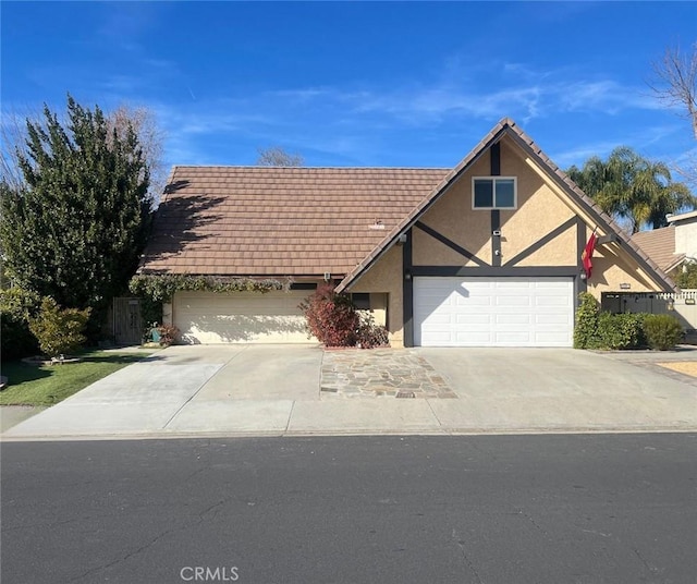 tudor-style house with an attached garage, concrete driveway, and stucco siding