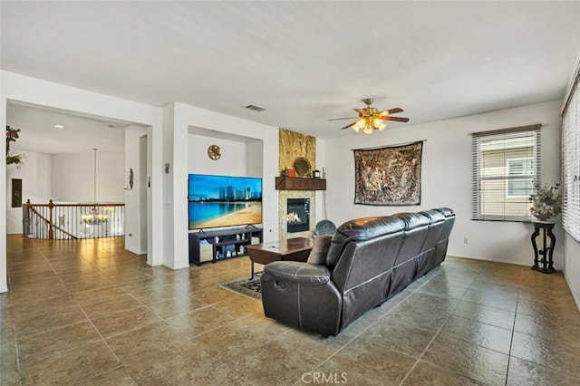 living room with a fireplace and ceiling fan with notable chandelier