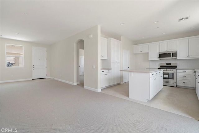 kitchen featuring white cabinetry, appliances with stainless steel finishes, a center island, and light carpet