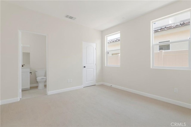 unfurnished bedroom with light colored carpet and connected bathroom