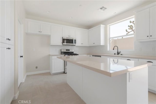 kitchen with light tile patterned flooring, sink, a kitchen island, stainless steel appliances, and white cabinets