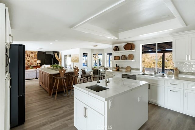 kitchen with a raised ceiling, sink, a center island with sink, and white cabinets