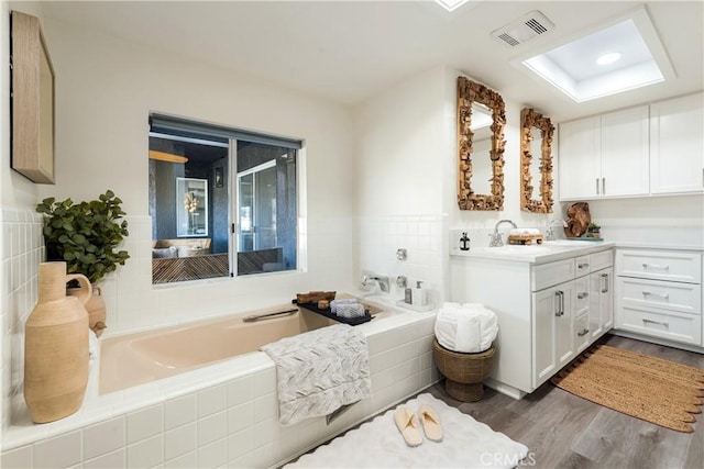 bathroom with wood-type flooring, a relaxing tiled tub, and vanity