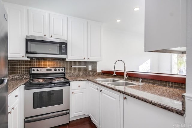 kitchen with white cabinetry, stainless steel appliances, sink, and dark stone countertops