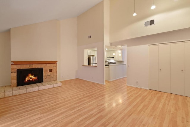 unfurnished living room with a tiled fireplace, high vaulted ceiling, and light hardwood / wood-style flooring