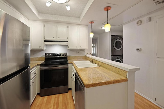 kitchen with pendant lighting, a raised ceiling, stacked washer and clothes dryer, kitchen peninsula, and stainless steel appliances