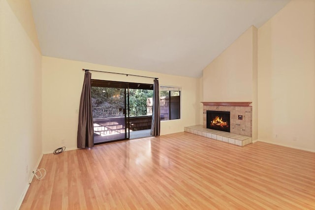 unfurnished living room featuring a tiled fireplace, high vaulted ceiling, and light hardwood / wood-style flooring