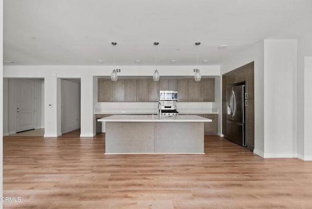 kitchen featuring a kitchen island with sink, hanging light fixtures, stainless steel appliances, and light hardwood / wood-style floors