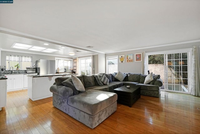 living room with sink, ornamental molding, and light wood-type flooring