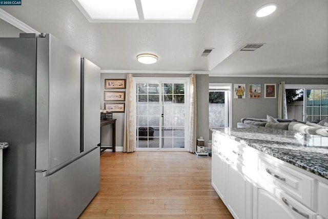 kitchen featuring stainless steel refrigerator, white cabinetry, dark stone counters, crown molding, and light wood-type flooring