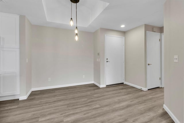 empty room featuring a tray ceiling and light wood-type flooring