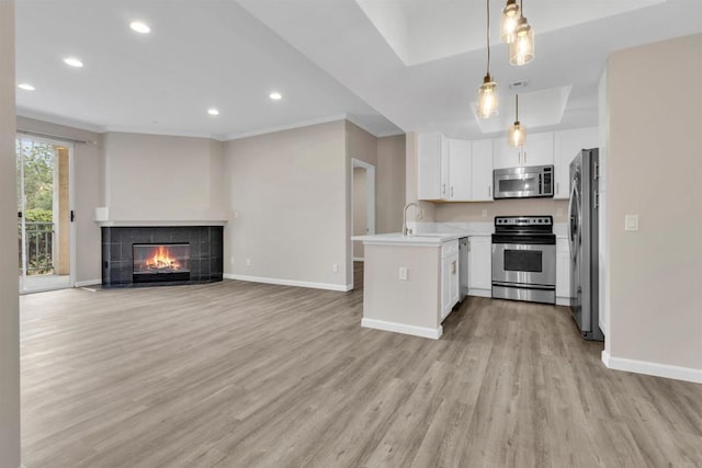 kitchen with appliances with stainless steel finishes, decorative light fixtures, white cabinetry, a tiled fireplace, and kitchen peninsula