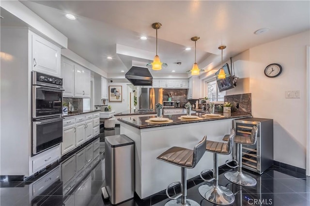 kitchen with tasteful backsplash, appliances with stainless steel finishes, a kitchen breakfast bar, kitchen peninsula, and white cabinets