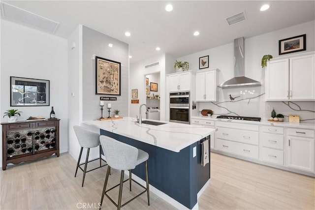 48 Vintage, Rancho Mirage, CA 92270 - kitchen with wall chimney exhaust hood, stainless steel double oven, a sink, light stone countertops, and a kitchen breakfast bar