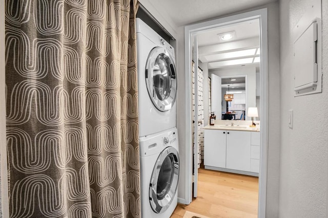 laundry area featuring stacked washing maching and dryer, sink, and light hardwood / wood-style floors