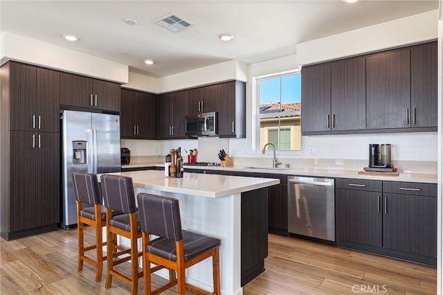 kitchen with a kitchen island, appliances with stainless steel finishes, a breakfast bar, sink, and dark brown cabinetry