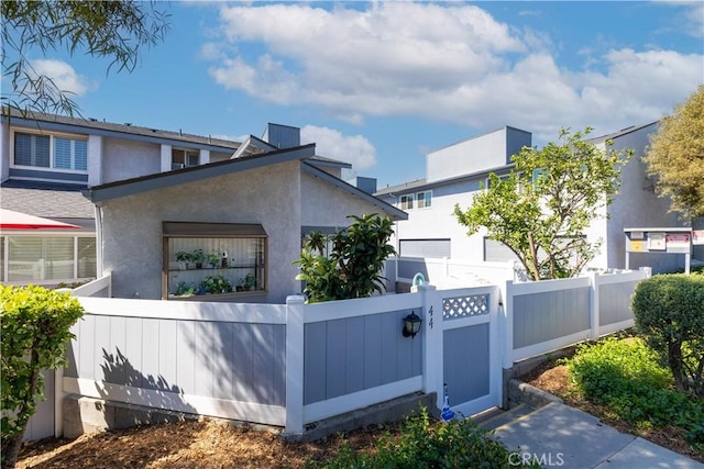 view of side of home featuring a fenced front yard, a gate, and stucco siding