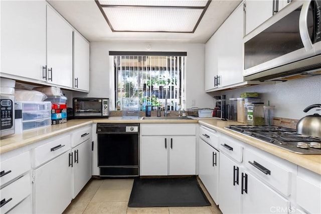 kitchen featuring light tile patterned flooring, a toaster, stainless steel appliances, white cabinetry, and light countertops