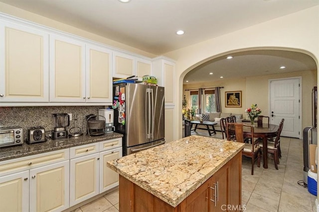 kitchen with a kitchen island, stainless steel fridge, white cabinets, and stone countertops