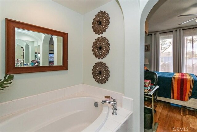 bathroom featuring a relaxing tiled tub, ceiling fan, and hardwood / wood-style floors