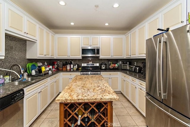 kitchen with appliances with stainless steel finishes, sink, dark stone countertops, decorative backsplash, and light tile patterned floors