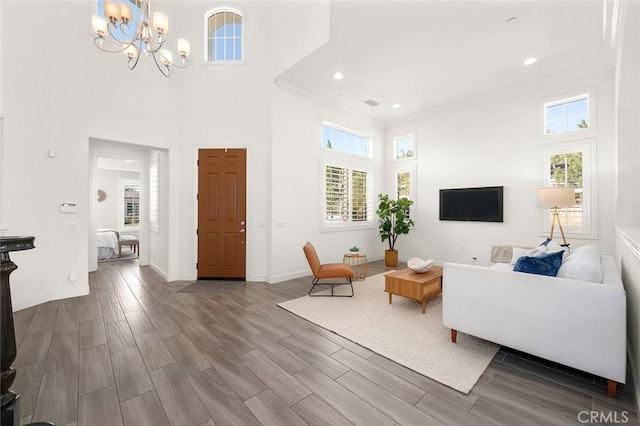 living room featuring a towering ceiling, plenty of natural light, a notable chandelier, and ornamental molding