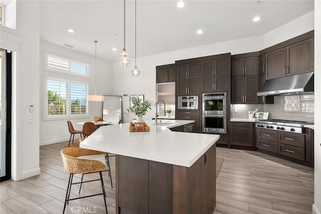 kitchen with sink, a breakfast bar area, appliances with stainless steel finishes, dark brown cabinets, and an island with sink